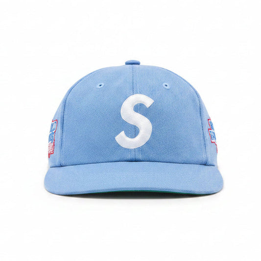 A light blue baseball cap featuring a large white embroidered letter 'S' on the front, with red and blue side patches, shown against a plain white background.