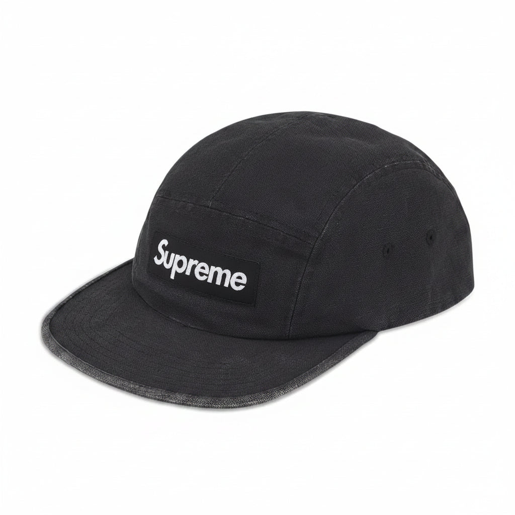 A black Supreme 5-panel camp cap with a white embroidered logo on the front patch, shown against a plain white background.