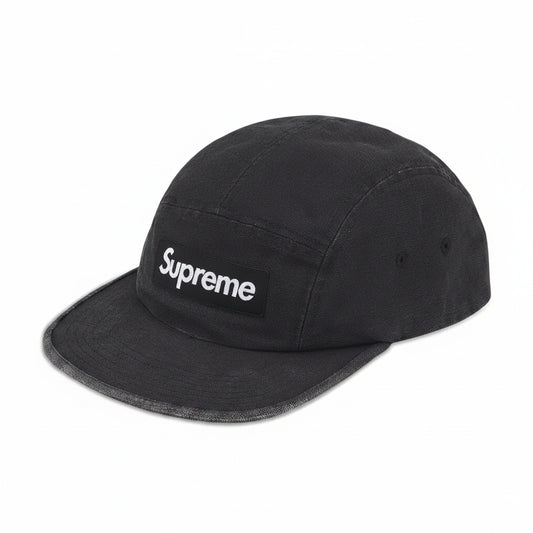 A black Supreme 5-panel camp cap with a white embroidered logo on the front patch, shown against a plain white background.